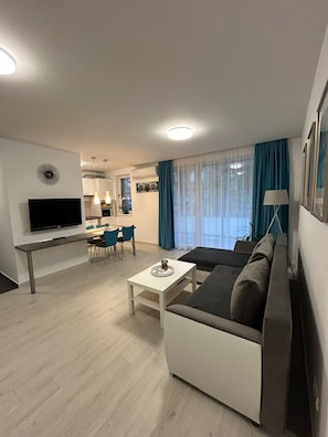 Een moderne woonkamer met een flatscreen televisie, een bank, een salontafel en een eethoek met stoelen en een tafel.