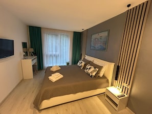 Hotellihuone, jossa on sänky, työpöytä, televisio ja ikkuna, jossa on verhot.