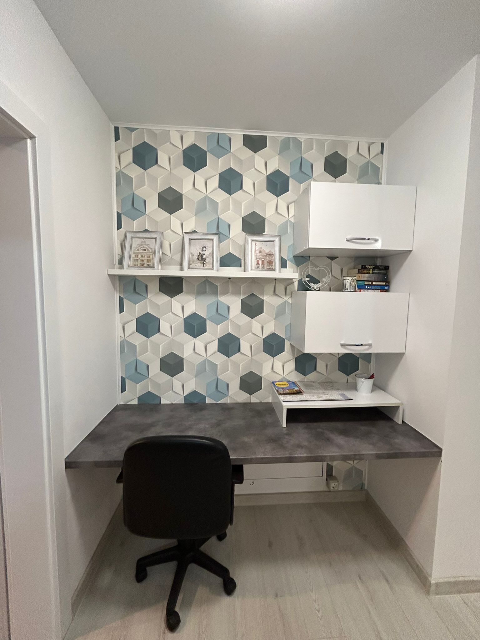 Un bureau d’angle avec un bureau, une chaise et une étagère, le tout placé contre un mur orné d’un motif géométrique.