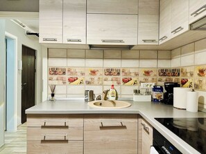 Uma cozinha moderna com armários de madeira clara, uma ilha central com pia e um revestimento de azulejos com desenhos de comida.