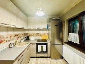 Cozinha moderna com forno embutido, geladeira de aço inoxidável e janela com vista para árvores.