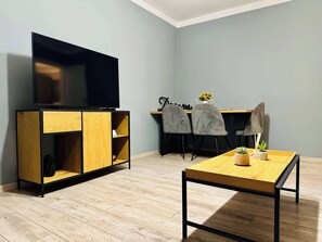 En moderne stue med et fladskærms-tv, træmøbler, et spisebord og grå polstrede stole.