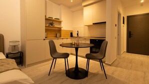 Habitación de hotel pequeña con cama, mesita de noche, mesa redonda con dos sillas, kitchenette y una puerta.