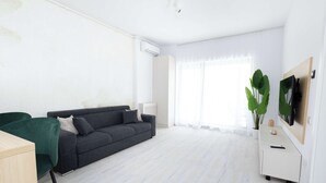 Een moderne woonkamer met een donkergrijze bank, een houten bureau en een witte kast.