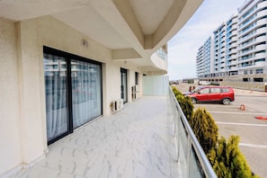 Ein modernes Gebäude mit Balkon, großen Fenstern und einem Parkplatz, auf dem ein rotes Auto steht.