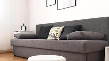 Una sala de estar moderna con un sofá gris, un taburete redondo pequeño y tres carteles motivacionales enmarcados en la pared.