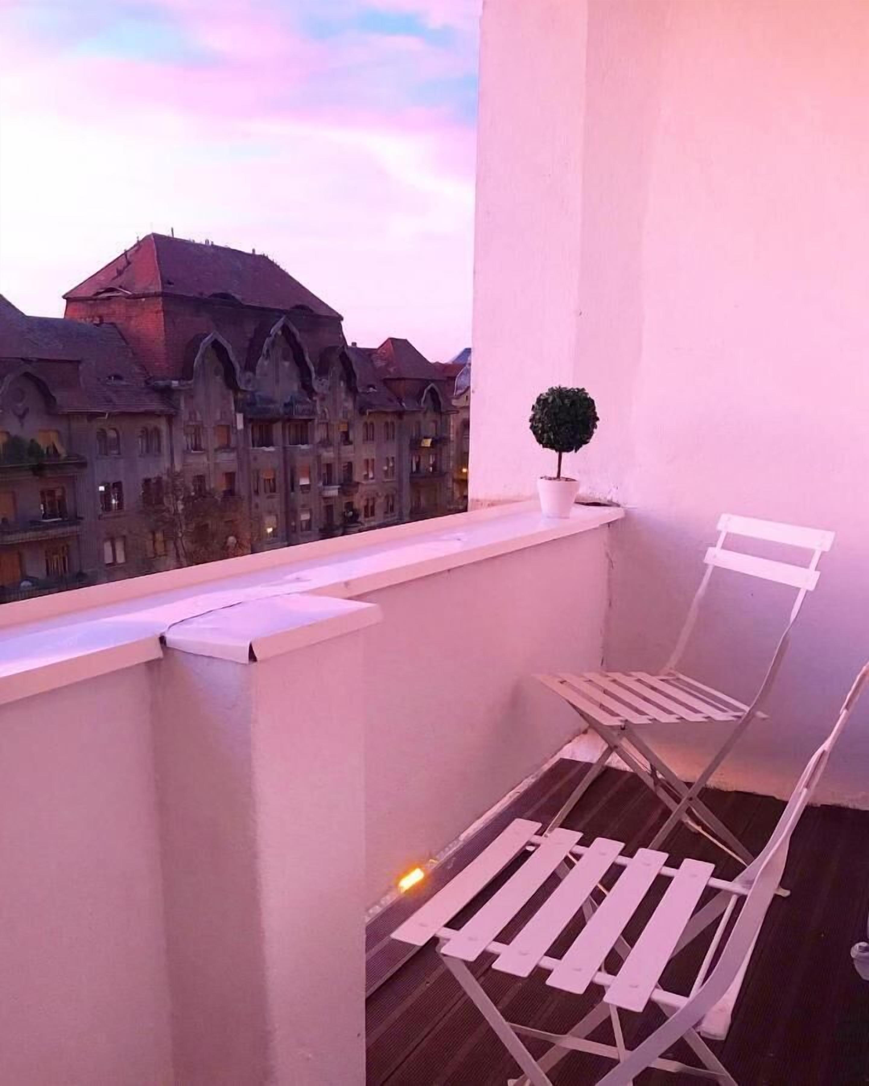 Un balcon avec une chaise blanche, une petite plante en pot et une vue sur des bâtiments historiques.