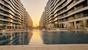 Een modern hotel met een centraal gelegen zwembad, meerdere balkons en uitzicht op de zonsondergang.