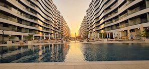 A modern hotel with a central swimming pool, multiple balconies, and a sunset view.