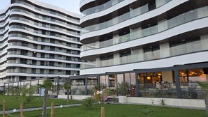 Een modern hotel met meerdere verdiepingen, gebogen balkons, terraszitplaatsen en een verzorgde tuin.