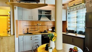 A modern kitchen with a dining area, a TV mounted on a wooden beam, and a window with curtains. - Joy City Stay Ultracentral Charming (Timișoara)