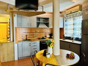 Eine moderne Küche mit Essbereich, einem an einem Holzbalken befestigten Fernseher und einem Fenster mit Vorhängen.