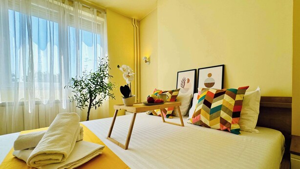 A hotel room with a bed, a table with a tray, a potted plant, and a window with curtains. - Joy City Stay Ultracentral Charming (Timișoara)
