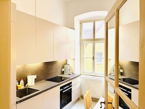 A modern kitchen with a black countertop, white cabinets, a window, and a radiator. - Joy City Stay  Unirii 4 (Timișoara)