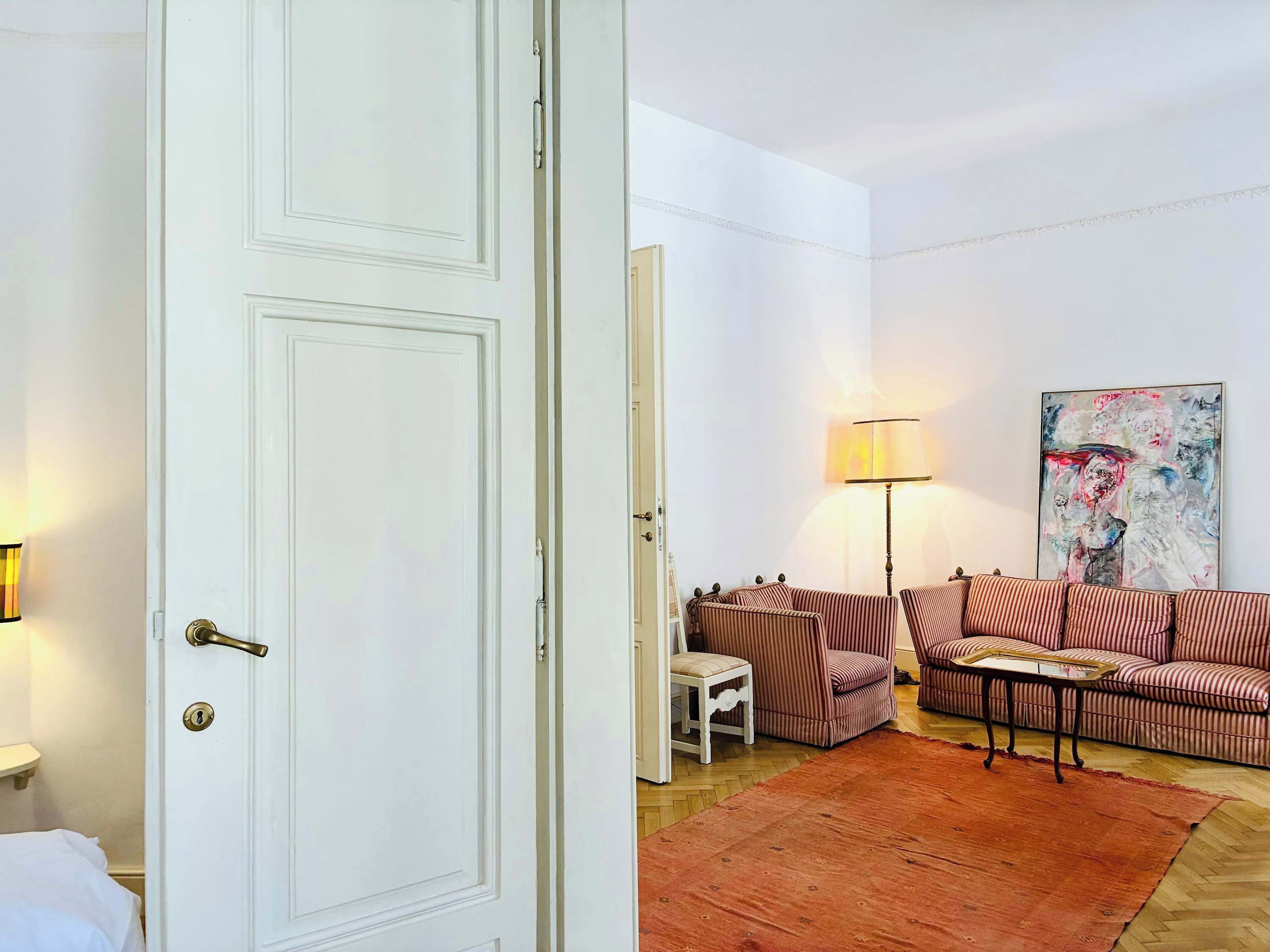 Ein Zimmer mit einer weißen Tür, einem gestreiften Sofa, einem kleinen Tisch und einer Lampe.
