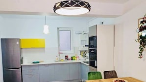 Une cuisine moderne avec des meubles gris, un mur d’accent jaune et un coin repas comprenant une table et des chaises en bois.