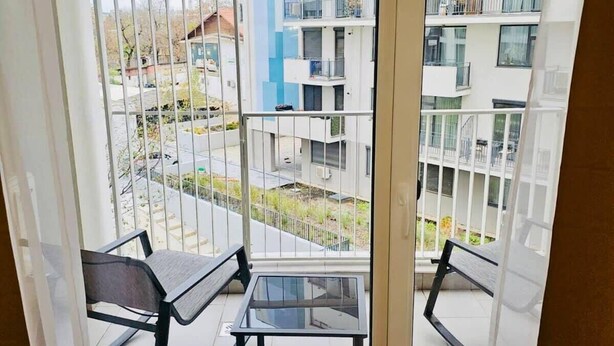 Un balcon doté d’une table en verre et de deux chaises, offrant une vue sur un quartier résidentiel avec des immeubles à plusieurs étages.