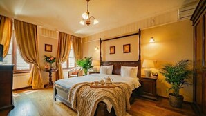 Een hemelbed met gordijnen, een nachtkastje met lamp, een potplant en een raam met gordijnen.