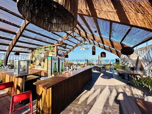 Een buitengedeeltelijk bar met houten constructie, zitplaatsen en uitzicht op zee.
