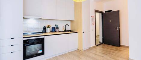 Una cocina moderna con armarios blancos, un horno negro, encimera de madera y una lámpara colgante.
