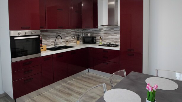 Una cucina moderna con pensili rosso scuro, forno in acciaio inossidabile, piano cottura a gas e zona pranzo con tavolo e sedie.