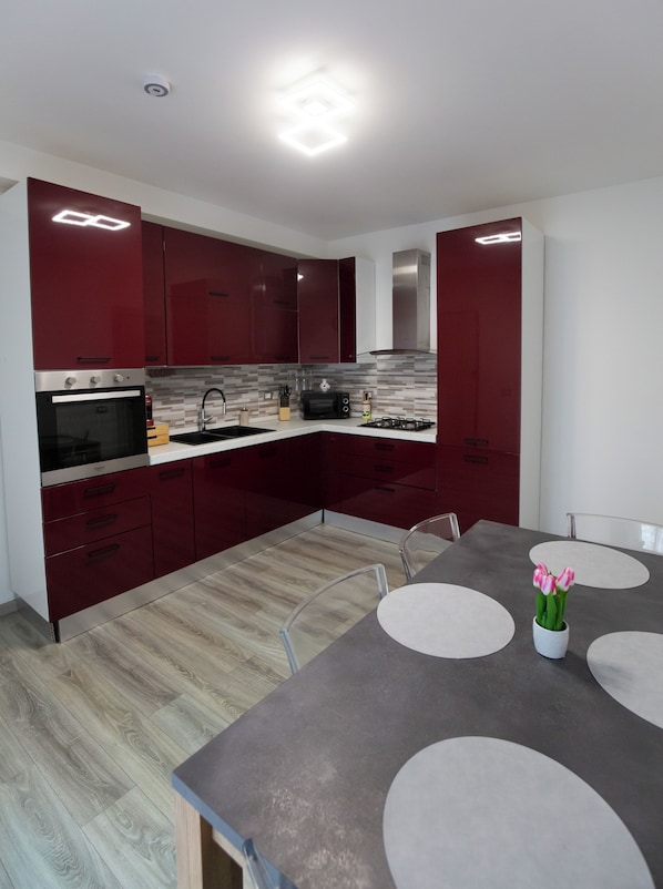 Une cuisine moderne avec des meubles de couleur rouge foncé, un four en acier inoxydable, une cuisinière à gaz et un coin repas comprenant une table et des chaises.