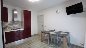 Una cucina moderna con un tavolo da pranzo, sedie, una televisione e un orologio appeso al muro.