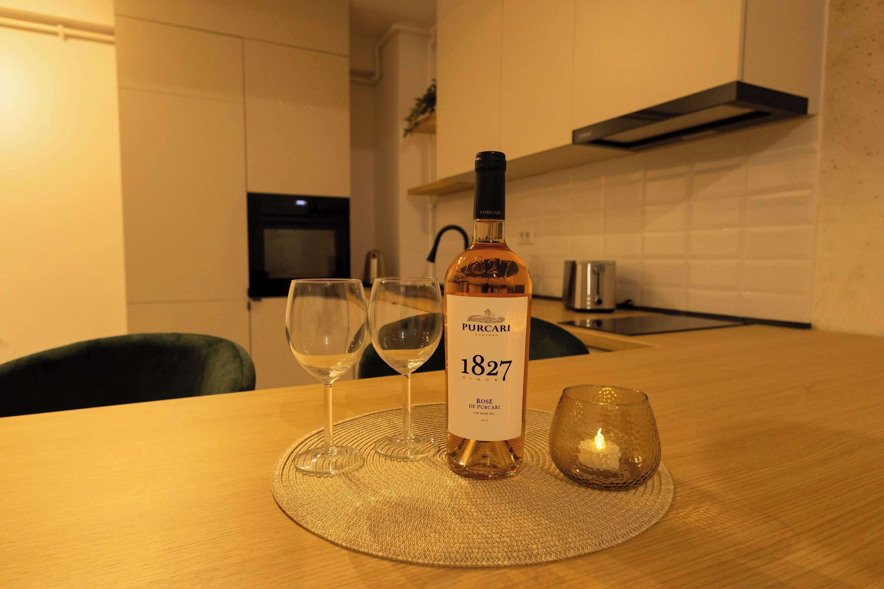 A bottle of wine, two glasses, and a candle on a table in a kitchen.