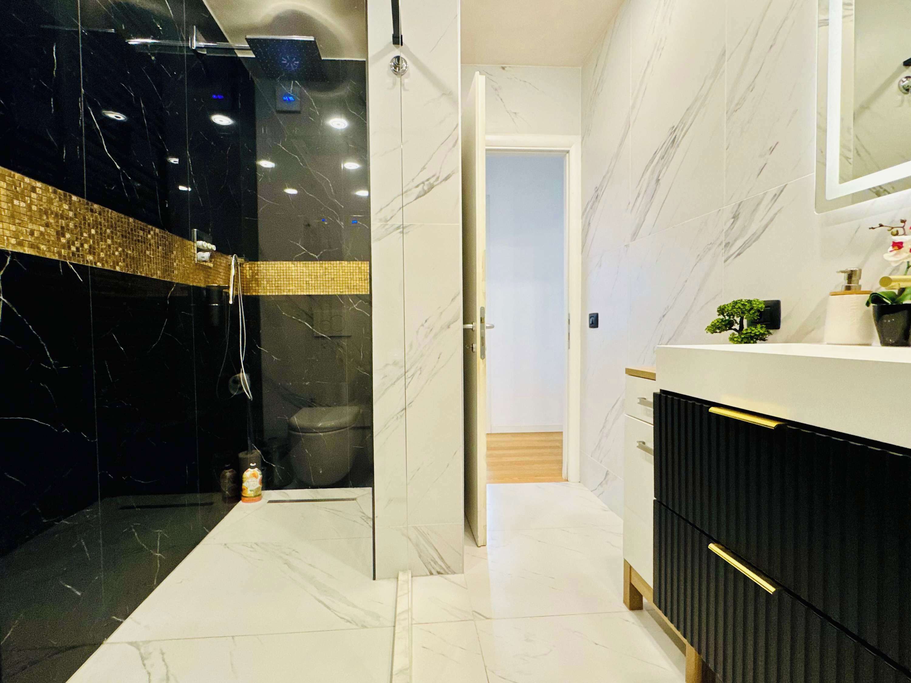 Un baño moderno con cabina de ducha de vidrio, tocador de mármol blanco y suelo de madera.