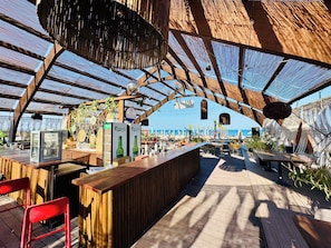 Un área de bar al aire libre con una estructura de madera, asientos y vistas al mar.