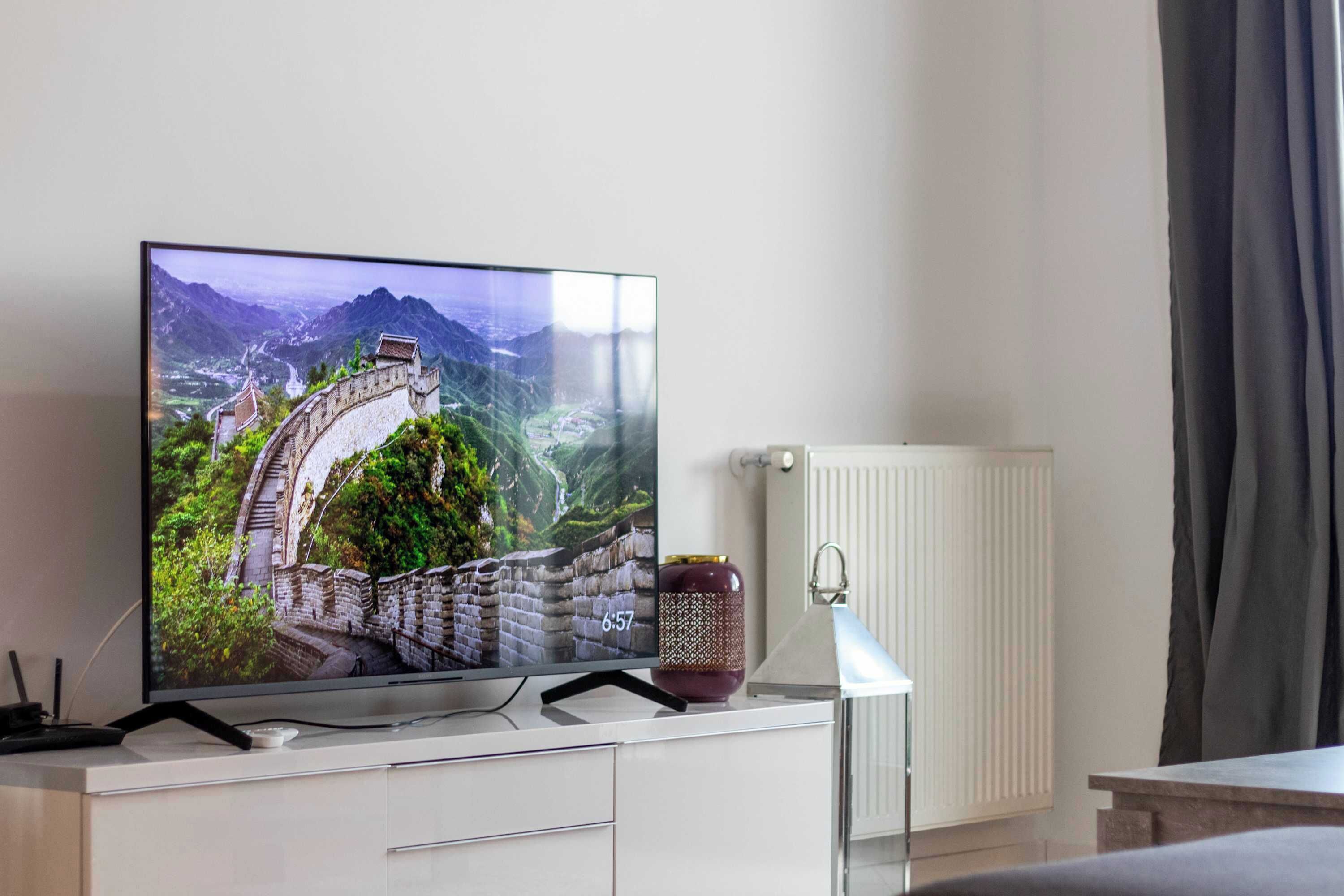 Un téléviseur à écran plat posé sur un meuble blanc, agrémenté d’un vase décoratif et d’une lampe.