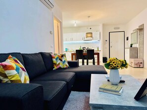Una sala de estar moderna con un sofá seccional, una mesa de centro con libros y un jarrón de girasoles, y vistas al área de la cocina.