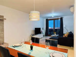 A modern living room with a dining area, a flat-screen TV, and a view of the cityscape through large windows. - Joy City Stay Fructus 30 (Timișoara)