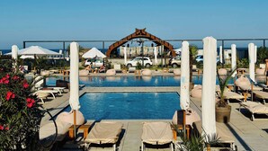 Zona de piscina con sillas de descanso, sombrillas y un arco decorativo.