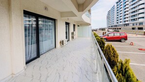 Een modern gebouw met balkon, grote ramen en een parkeerplaats met een rode auto.