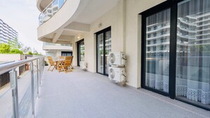 Een balkon met buitenmeubilair, airconditioners en uitzicht op een hoog gebouw.