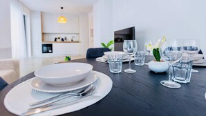 Een eettafel gedekt met borden, bestek en glazen, met een moderne keuken en woonkamer op de achtergrond.