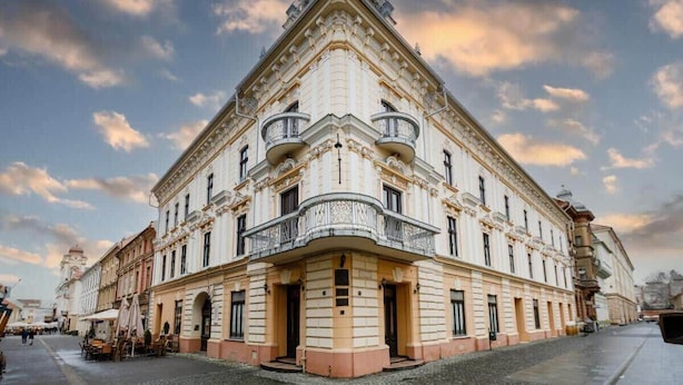 Un edificio histórico con arquitectura ornamentada, una entrada en esquina y una calle adoquinada.