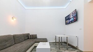 Una sala moderna con un sofá modular, una mesa de centro blanca, un televisor montado en la pared y un tragaluz.