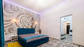Un dormitorio con una cama azul, un adorno en la pared y una mesita de noche blanca.