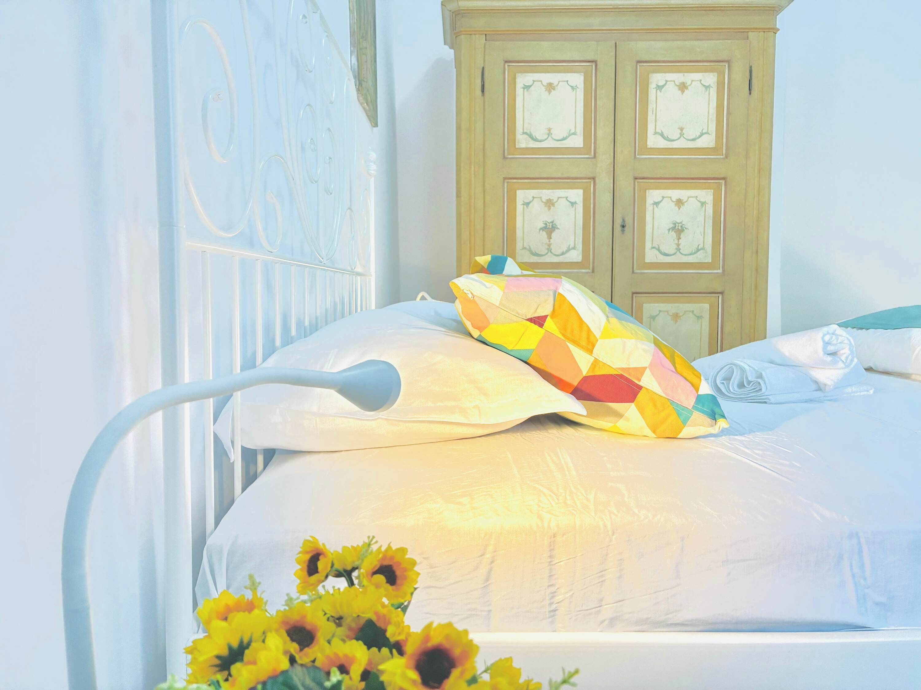 Un lit avec une tête de lit blanche, un coussin coloré et une couverture blanche.