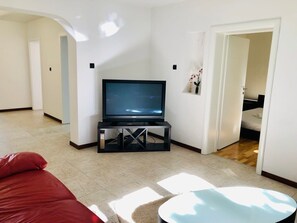 A living room with a flat-screen TV on a black stand, a red sofa, and a small round table. - Joy City Stay George 12 (Timișoara)