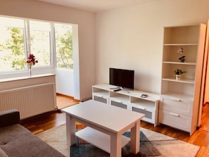 A modern living room with a white TV stand, a flat-screen TV, a white coffee table, and a bookshelf. - Joy City Stay Martir Miroslav 15 (Timișoara)