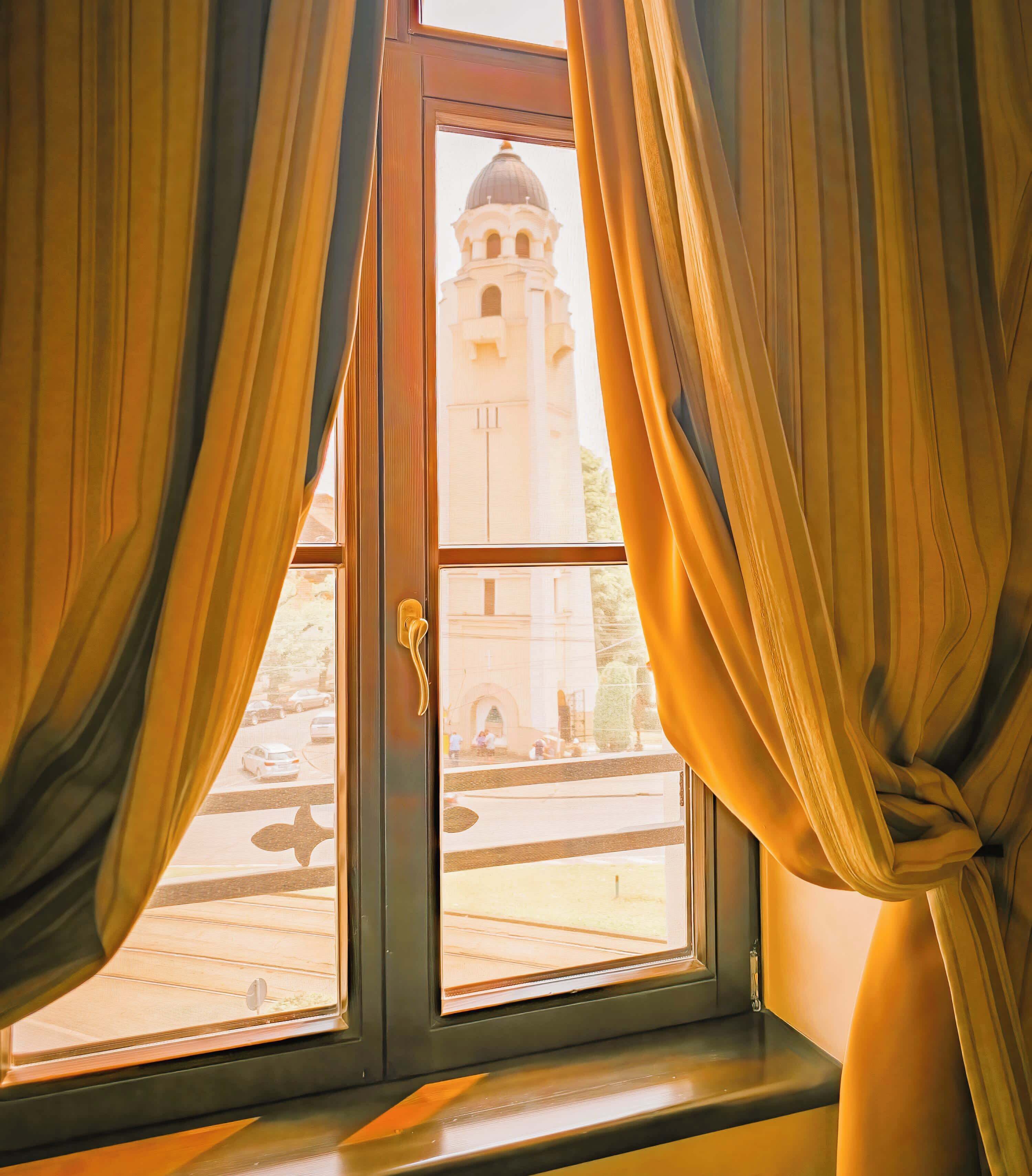 A window with curtains, a view of a building with a dome, and a street scene.