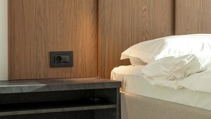 Une chambre à coucher avec une armoire en bois, une table de chevet avec une télécommande et un lit avec du linge de lit blanc.