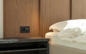 Un dormitorio con un armario de madera, una mesita de noche con control remoto y una cama con ropa de cama blanca.