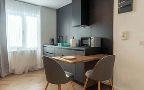 Een kleine keuken met een magnetron, koffiezetapparaat en een klein spoelbakje. Er zijn twee stoelen en een houten tafel.