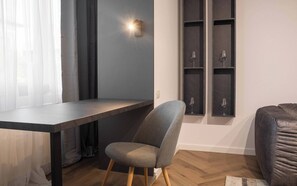 Een moderne kamer met een donker houten bureau, een grijs gestoffeerde stoel en een ingebouwde wijnrek met glazen.