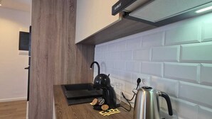 Moderni keittiö, jossa on puinen työtaso, musta induktioliesi, vedenkeitin ja seinälle asennettu liesituuletin.