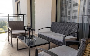 Un balcón con mobiliario de mimbre, una mesa de vidrio y un candelabro.